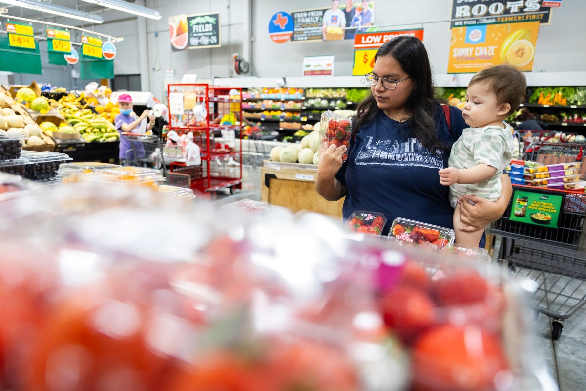 Jaqueline Hernandez and her 11-month-old son study containers of strawberries at a north Houston grocery store on Tuesday, Aug. 12, 2025.
